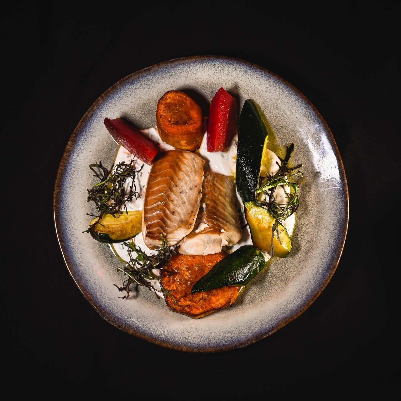Pavé de saumon, patate douce et courgettes rôties, dressés dans une assiette en grès