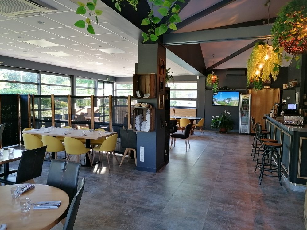 La salle du Au19 : tables en bois clair, chaises jaunes, suspensions végétales et le bar, devant les baies vitrées